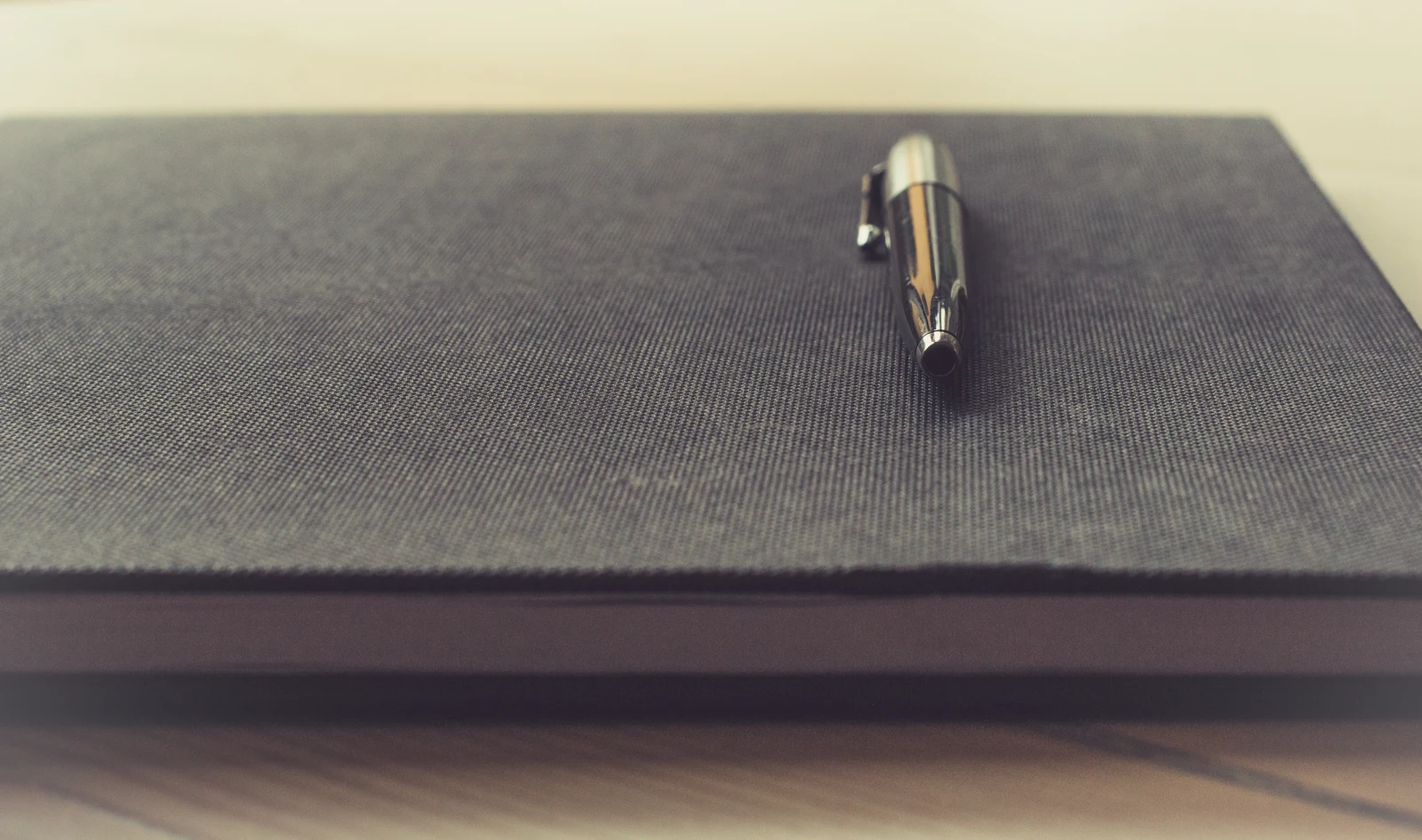 A closed notebook with a pen resting on its cover.