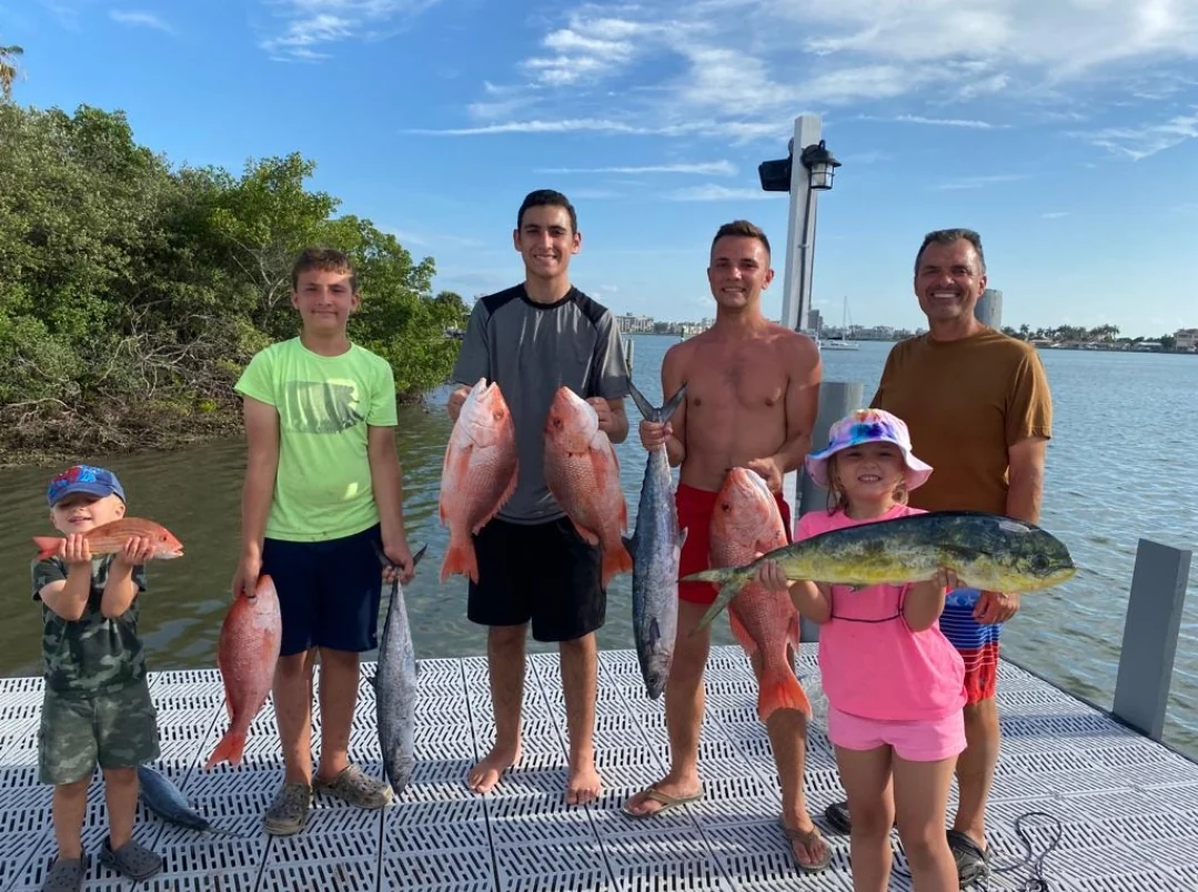 A group of anglers of different ages displaying their catches on a dock.