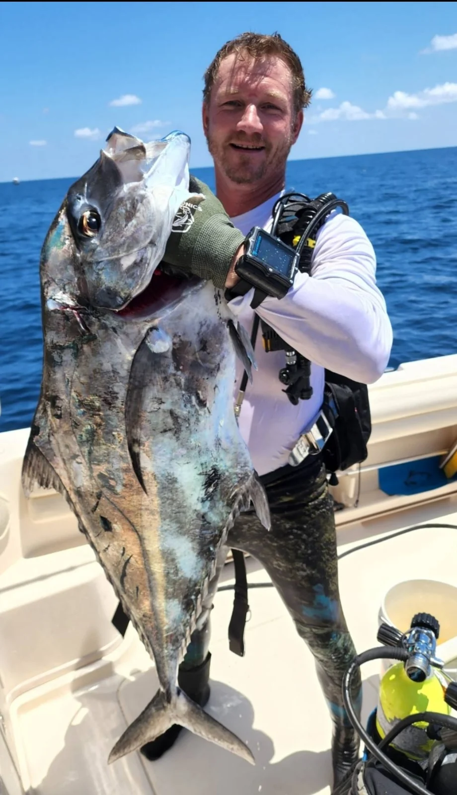 An angler in diving equipment holds a large retained silver fish aboard a boat; species, place and diving method are unconfirmed.