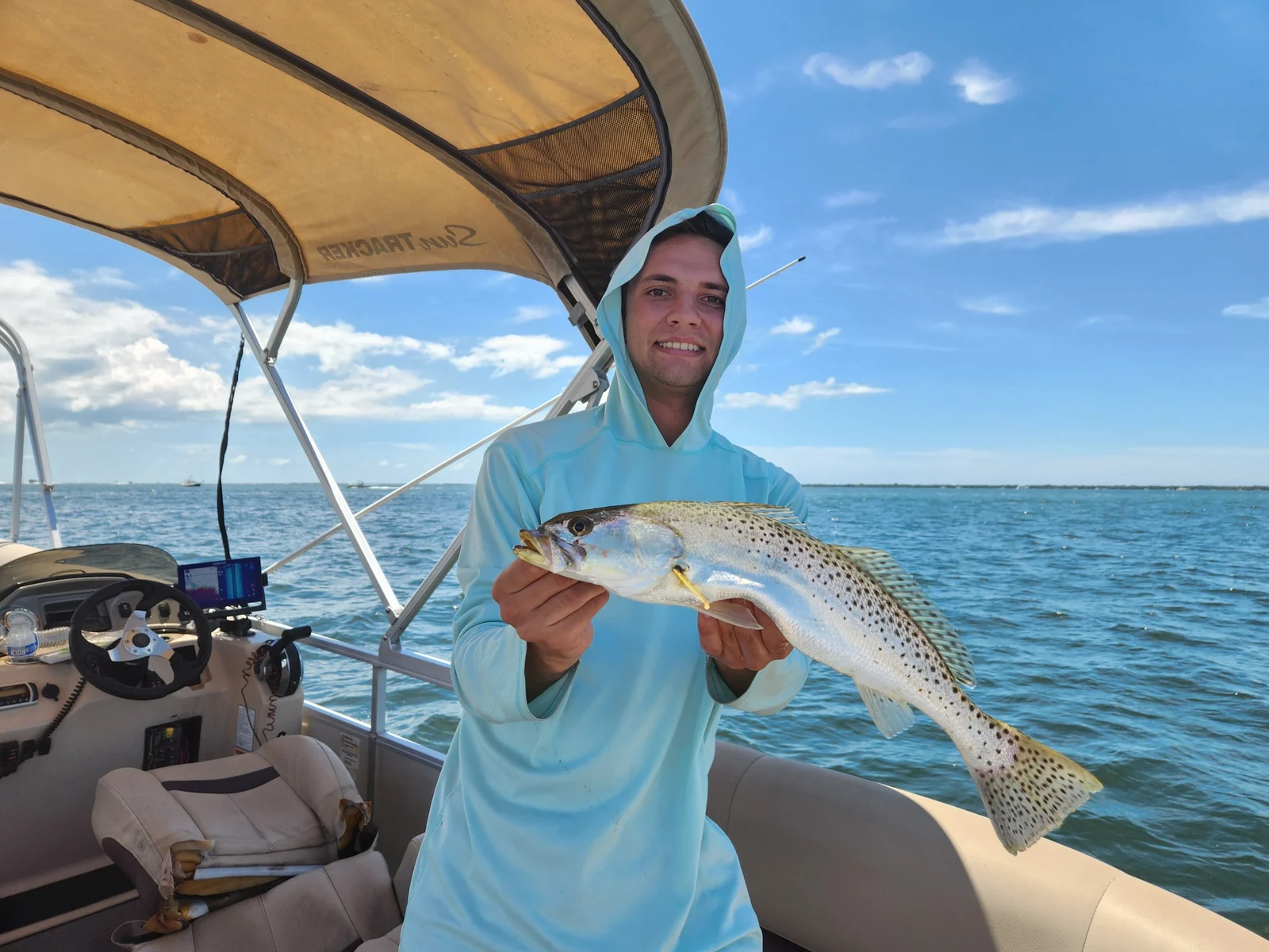 An angler holding a spotted fish aboard a small boat on blue coastal water.