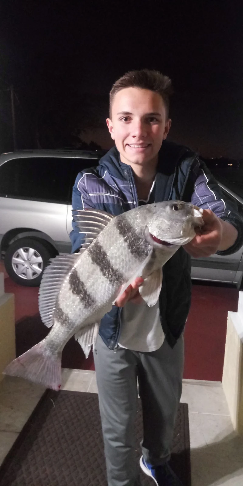 An angler holding a black drum with dark vertical bars; owner-confirmed species, catch location and date unconfirmed.